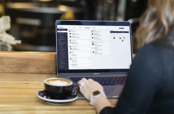 An image shot from behind, showing a person sitting at a laptop with a cup of coffee.