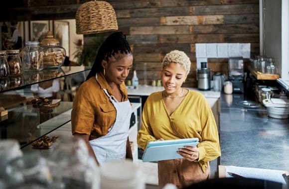 An image of two employees standing behind the counter of a cafe, looking at a tablet.