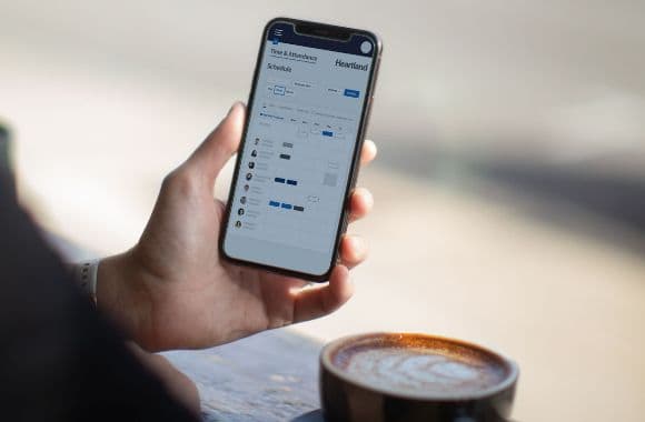 An image of a hand holding a phone above a cup of coffee.